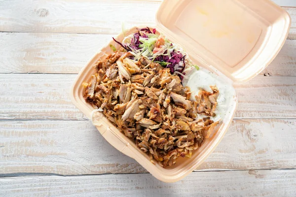 Fast food in a take away box from styrofoam, doner kebab with chicken meat, salad and dip on a wooden table, copy space, high angle view from above, selected focus