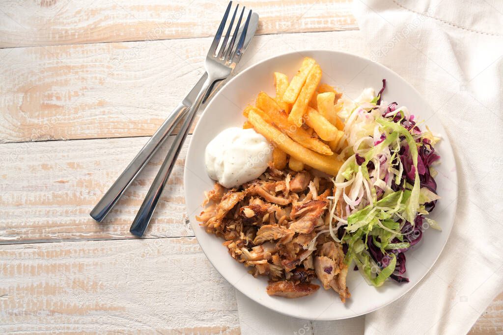 Doner kebab chicken meat with french fries, salad and tzatziki dip, fast food plate on a wooden table, copy space, high angle view from above, selected focus