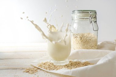 Vejetaryen yulaf ezmesi, içme bardağına su sıçratır ve beyaz bir peçeteyle birlikte açık ahşap bir masada saklama kavanozu, sağlıklı laktozsuz ve süt ürünü içermeyen alternatif, kopyalama alanı, seçilmiş odak, dar alan derinliği.