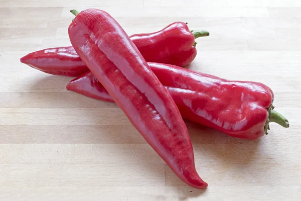 Three red sweet pointy peppers (capsicum) on a wooden board — Stock Photo, Image