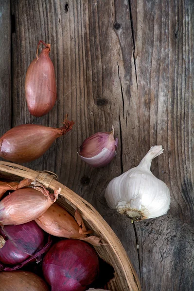 Cibuli a česnek v košíku na tmavé dřevo — Stock fotografie