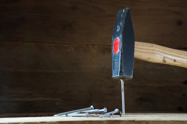 Martillo golpeando un clavo, fondo de madera oscura con copyspace — Foto de Stock