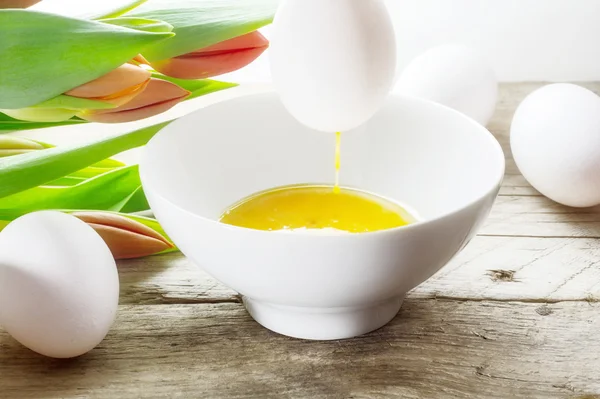 Soffiare le uova per la decorazione di Pasqua, tulipani sullo sfondo — Foto Stock