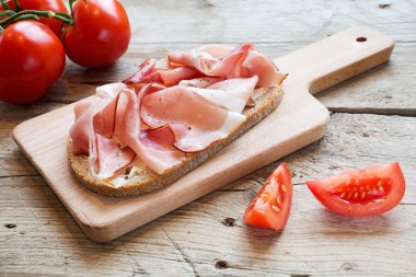 bir ahşap tahta üzerinde jambon pastırmalı doyurucu ekmek