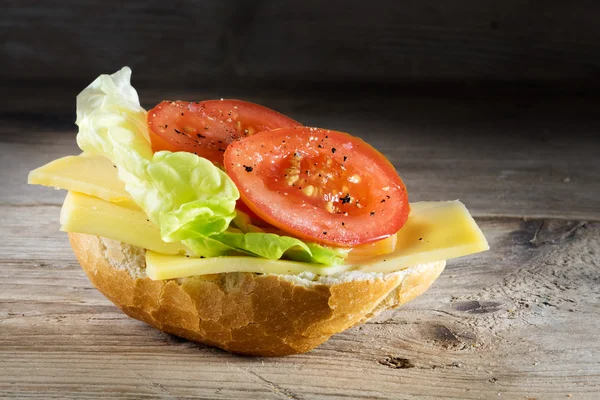 Semmel mit Käse, Salat und Tomaten auf rustikalem Holz, dunkel — Stockfoto