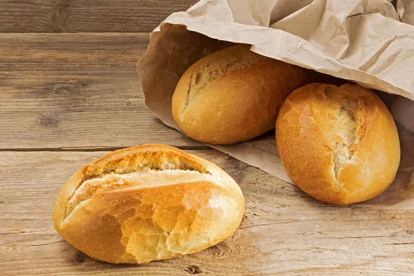 Bread rolls in a paper bag on a rustic wooden table — Stock Photo, Image
