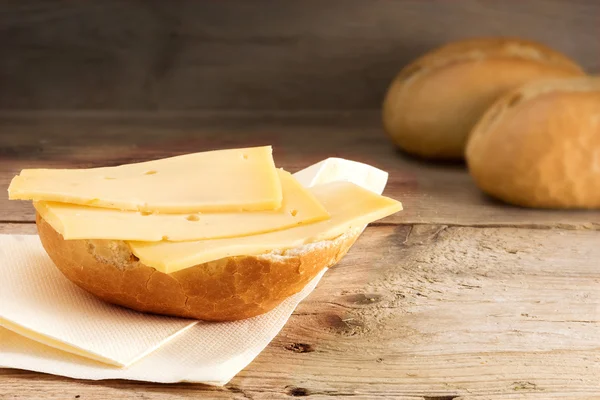 Bun with cheese and blurry bread rolls in the background on wood — Stock Photo, Image