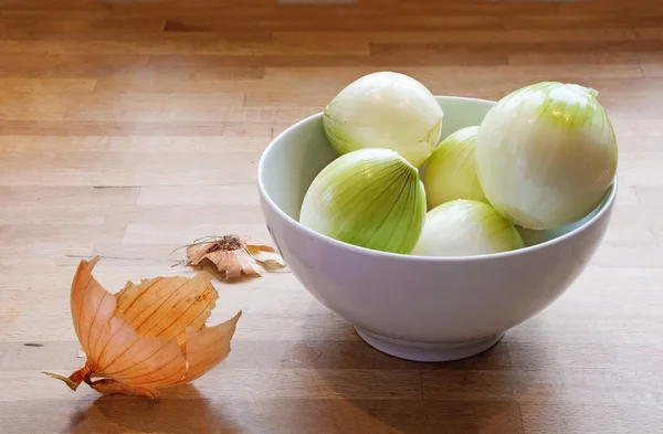 Oloupané cibule v misce a cibule oloupeme na dřevo — Stock fotografie