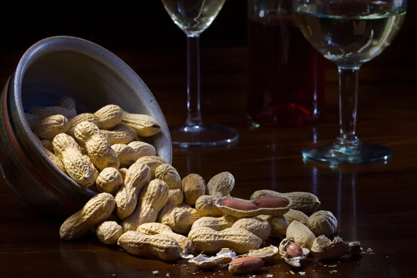 Jordnötter i en keramikskål och på ett mörka träbord, vin glas — Stockfoto