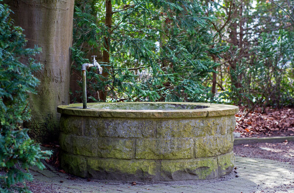 round water well  with faucet in a cemetery with old trees
