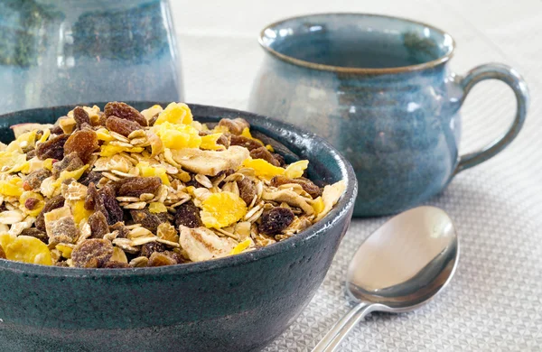 Muesli in een blauwe kom, keramische mokken op de achtergrond — Stockfoto