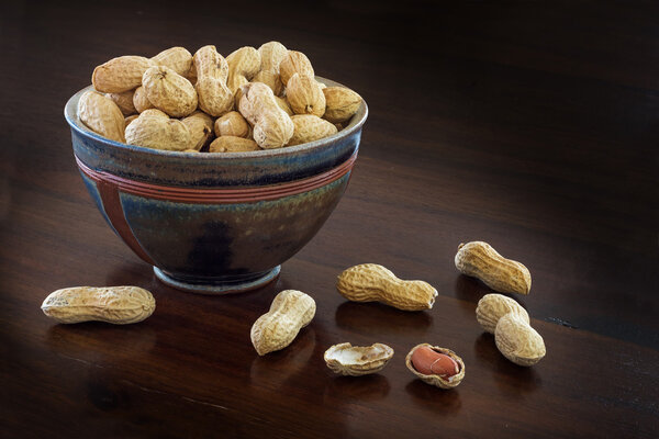 peanuts in a ceramic bowl on a dark brown table, copyspace