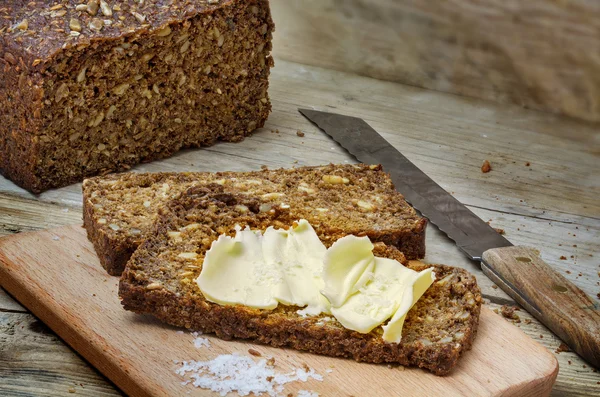 Donkere roggebrood met zaden, boter en zout op rustieke hout — Stockfoto