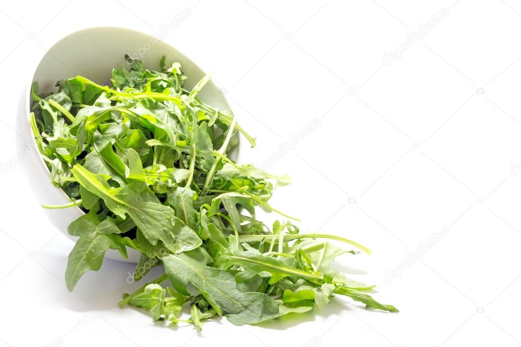 rocket salad leaves, rucola or arugula, falling from a ceramic b