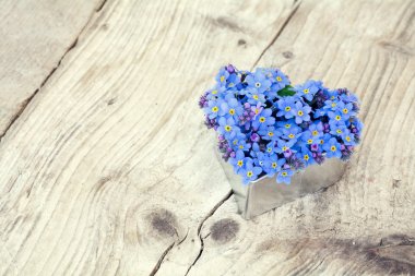 Heart shape with forget-me-not flowers on  rustic wood
