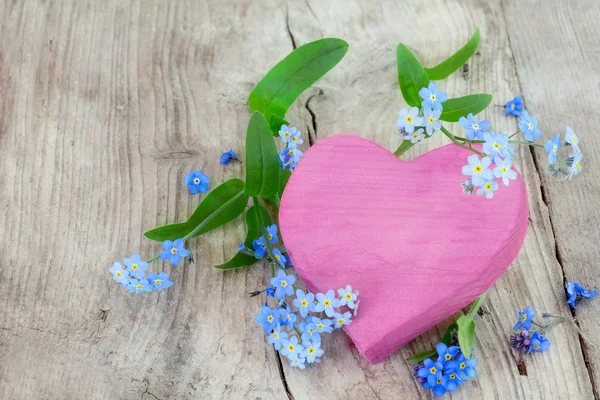 Pink heart shape made of wood with forget-me-not flowers on a wo — Stock Photo, Image