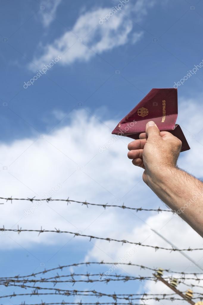 man's hand holding his passport as a paper airplane  over a barb