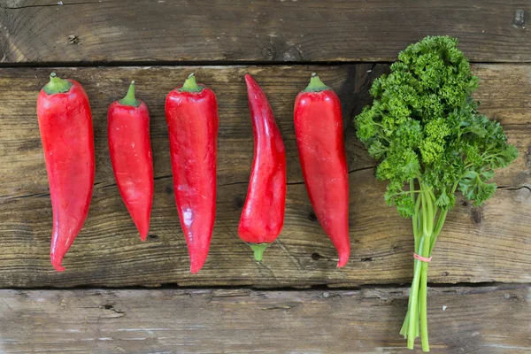 Red sweet pointed peppers in a row and parsley on rustic wood — 图库照片