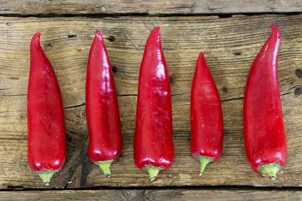 Red sweet pointed peppers in a row on rustic wood — 图库照片