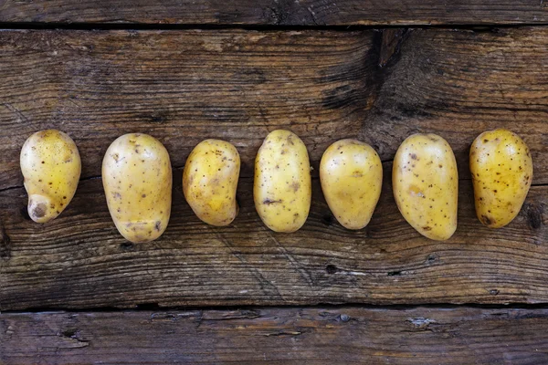 Young potatoes in a row on a dark rustic wooden — Stock Photo, Image