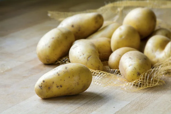 Papas nuevas en un tablero de cocina de madera — Foto de Stock