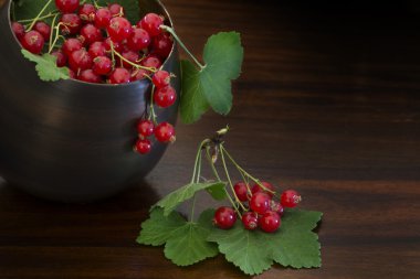 red currants and leaves in a bowl on dark brown wood