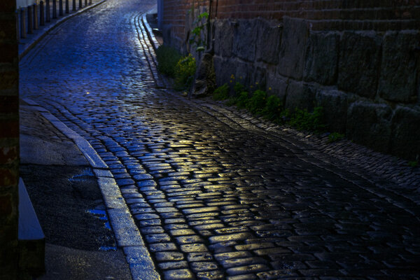 Alley with wet cobblestones at night in an old town, narrow depth of field