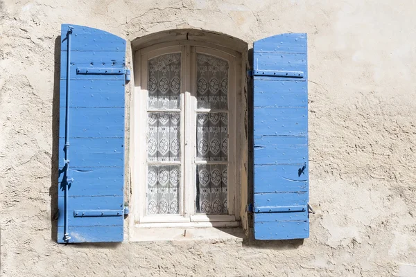 Old window with blue shutters and lace curtain in a rough-plaste — Stock Photo, Image