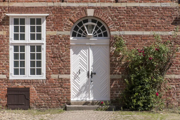 Voordeur, spiegelbevestiging windows en klimmen rose op een typische baksteen — Stockfoto