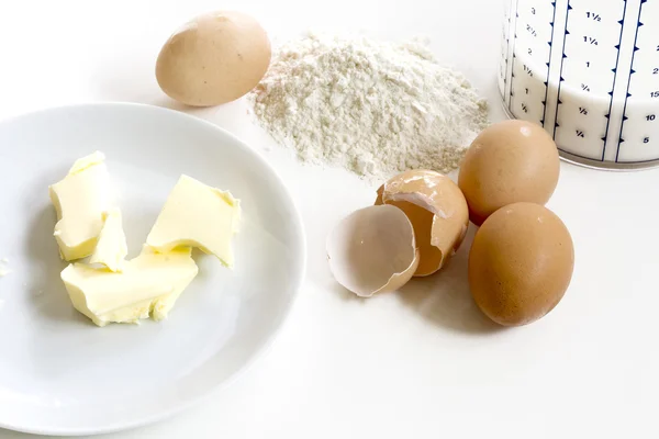 Bakken ingrediënten, boter, eieren, meel en melk op een witte achterzijde — Stockfoto