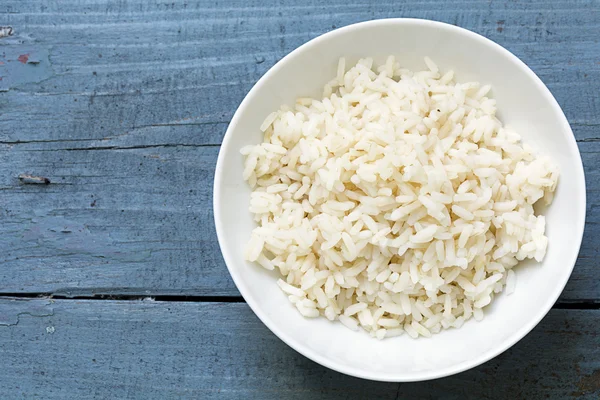 Arroz cozido em uma tigela de porcelana branca em madeira azul rústica — Fotografia de Stock