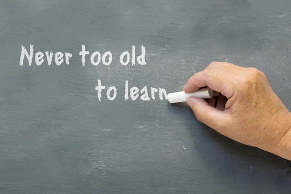 Older hand writes on a chalkboard: Never too old to learn — Stock Photo, Image