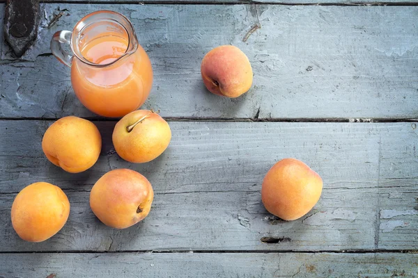 Abricots frais et jus dans une cruche en verre sur woo rustique gris-bleu — Photo