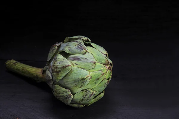 Natural artichoke on very dark wood, background fade to black — Stock Photo, Image