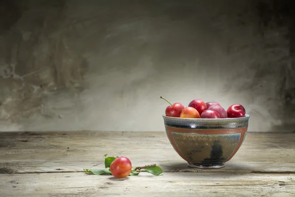 Divoké červené švestky v keramické misce na starý dřevěný stůl — Stock fotografie