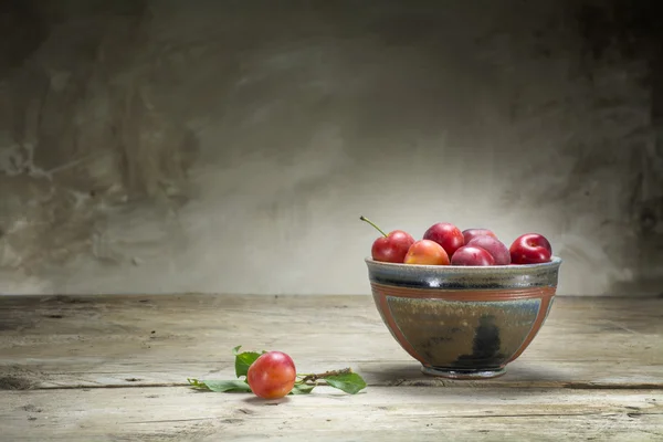 Prunes rouges sauvages dans un bol de poterie sur une vieille table en bois — Photo