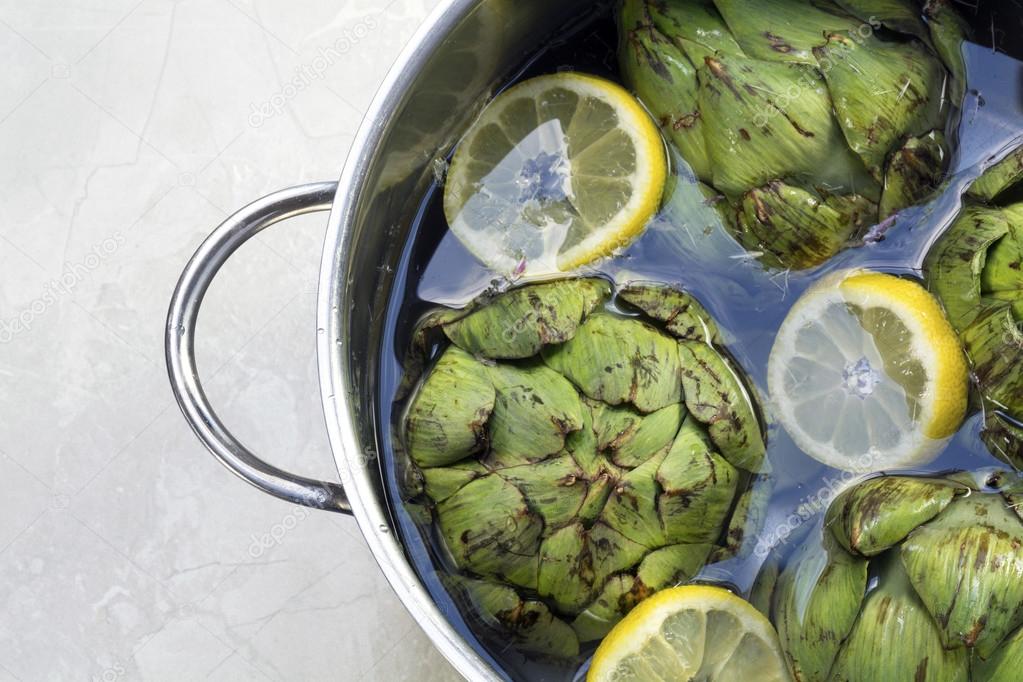 artichokes with lemon slices and water in a stainless  pot