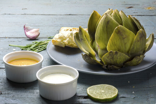 приготовленный артишок с соусом и хлебом на деревенской серой синей древесине
