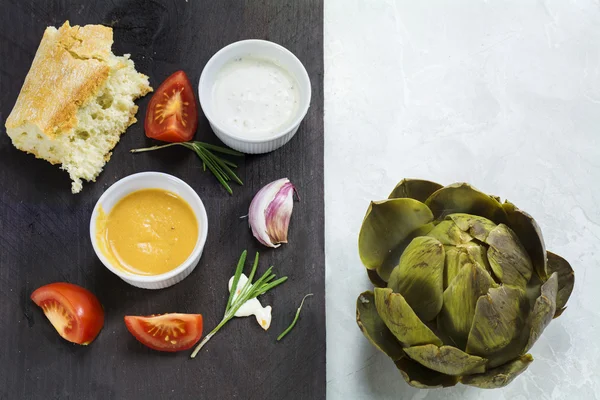 Cooked artichoke with dips and ingredients, background half dark — Stock Fotó