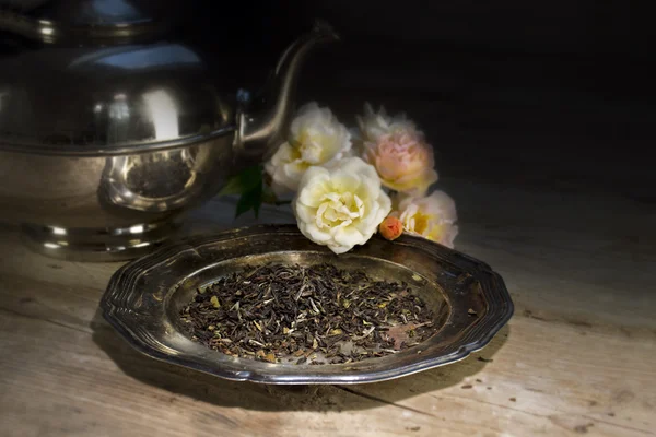Loose black tea on an old dish, roses and silver teapot — 图库照片