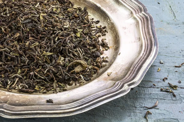 Loose black Darjeeling Tea on a silver plate on rustic blue pain — Stock Photo, Image