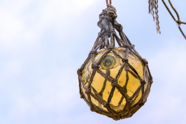 Historical yellow glass fishing float ball hanging in a net to d clipart