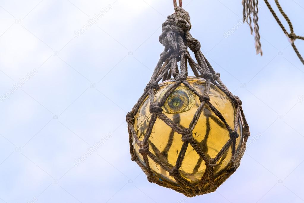 Historical yellow glass fishing float ball hanging in a net to d