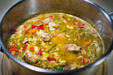 Paslanmaz çelik bir tencerede domuz eti ve dolma biberli fasulye güveci, kırsal ev yapımı yemek veya önceden pişirilmiş gıda depolama, seçilmiş odak, dar alan derinliği