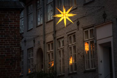 Aydınlatılmış Moravya yıldızı eski bir kasaba evinde asılı duruyor, Lubeck şehrinin dar sokağının camlarında yansımalar var, kopyalama alanı, seçilmiş odak alanı, dar alan derinliği.