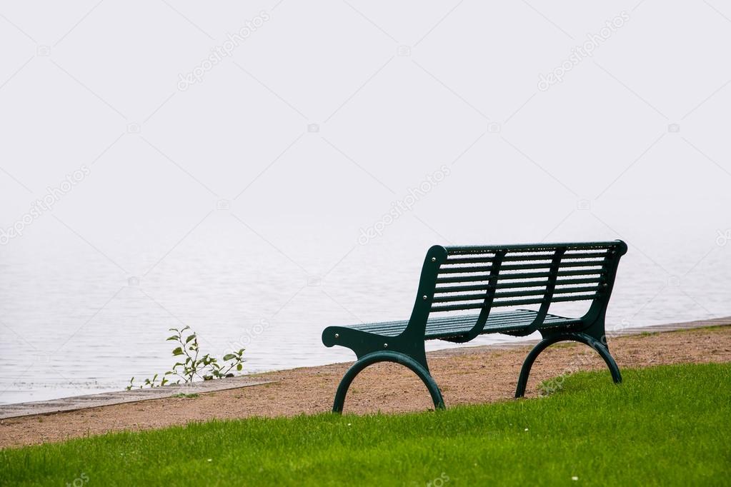 empty park bench, wet from the rain on the shore of a misty lake