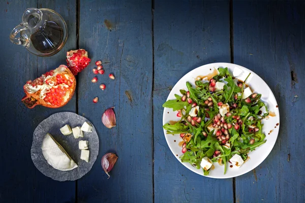 Ensalada de rúcula con queso y granada sobre madera rústica, ver fr — Foto de Stock