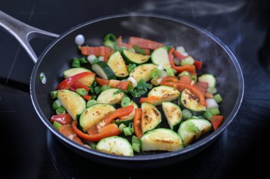 Sebzeler siyah bir tavada sotelenmiş, kızarmış kabak, kırmızı dolma biber şeritleri ve yeşil soğan, sağlıklı bir vejetaryen ya da vejetaryen diyeti için hızlı kızartma tabağı, seçilmiş odaklanma, dar bir tarla