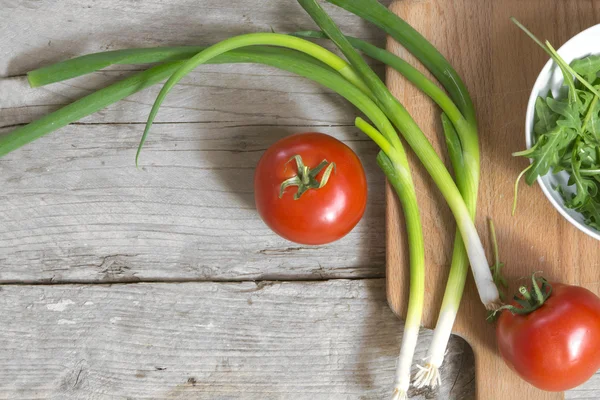 Tomatoes, spring onions and arugula on a rustic wooden table — Stock Image Tomatoes, spring onions and arugula on a rustic wooden table Stock Picture