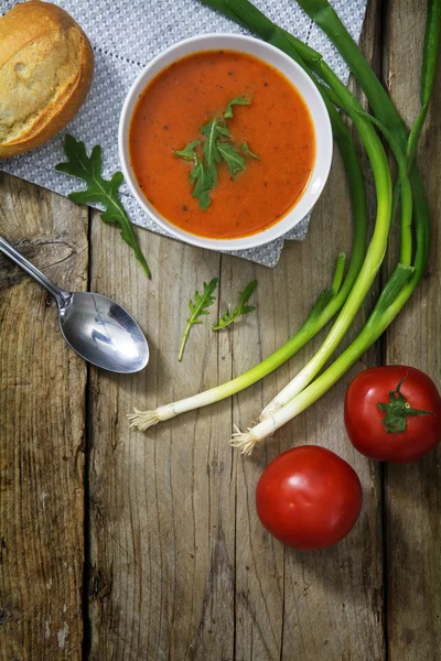 Tomato soup with bun, green onions and arugula garnish on rustic — Stock Image Tomato soup with bun, green onions and arugula garnish on rustic Royalty Free Stock Photos